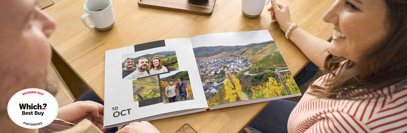 A person is flipping through an open photo book with pictures of holiday destinations and friends on a wooden table