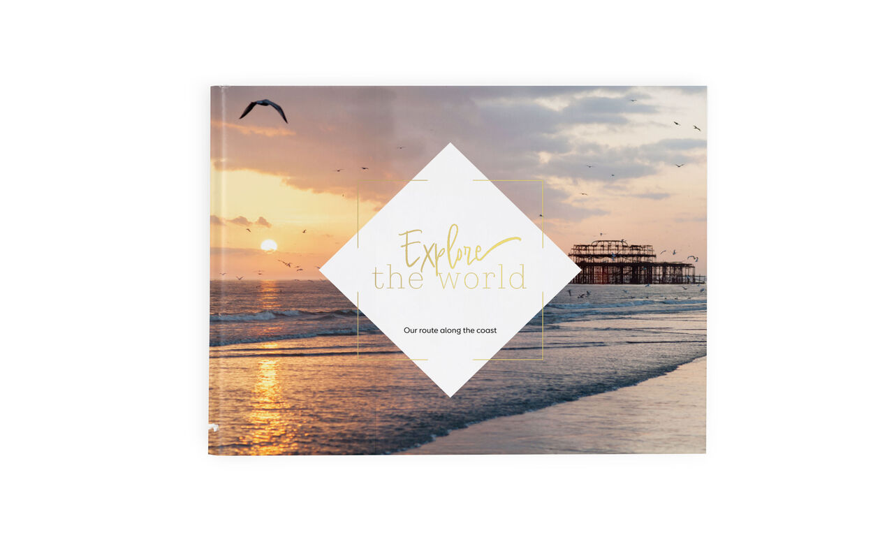 An open photo book titled “Explore the World” on a table, with a sunset by the sea in the background.