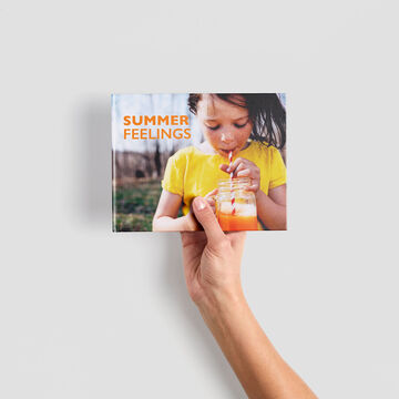 A hand holds a CEWE photo book titled "Summer Feelings."
