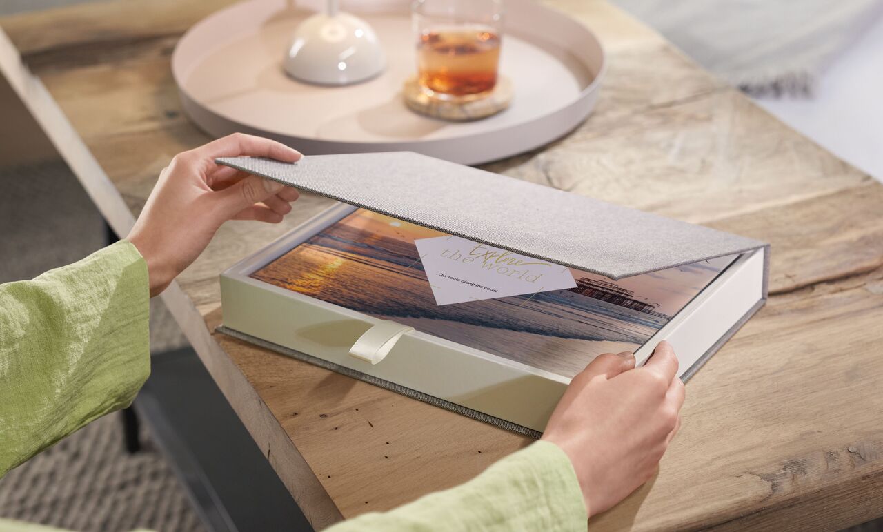 A person opens a CEWE photo book box with a beautiful picture and a greeting card on it