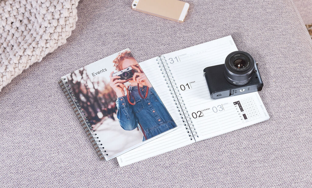 A CEWE photo book and a camera lie on a light sofa.