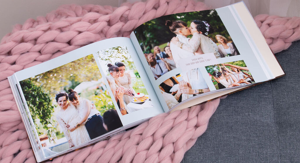 An opened CEWE PHOTO BOOK with loving photos from a festive occasion, surrounded by fluffy fabric.