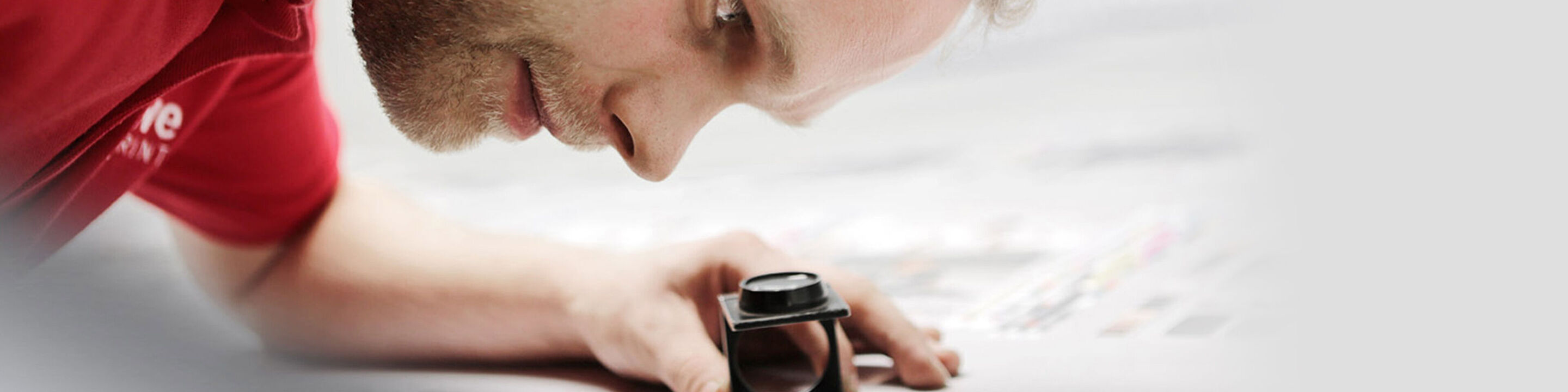 An employee from CEWE carefully checks the print of a photo using a magnifying glass.