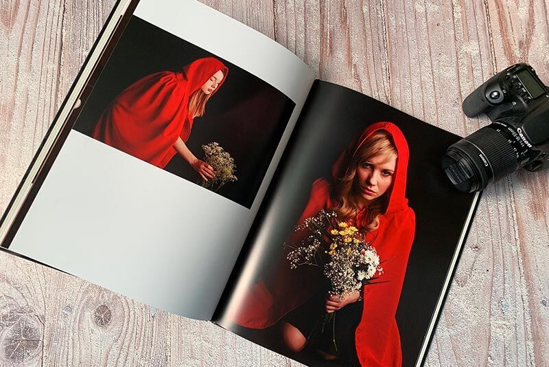 A person in a red cloak holds flowers in their hand. They stand in front of a photo book with other images.