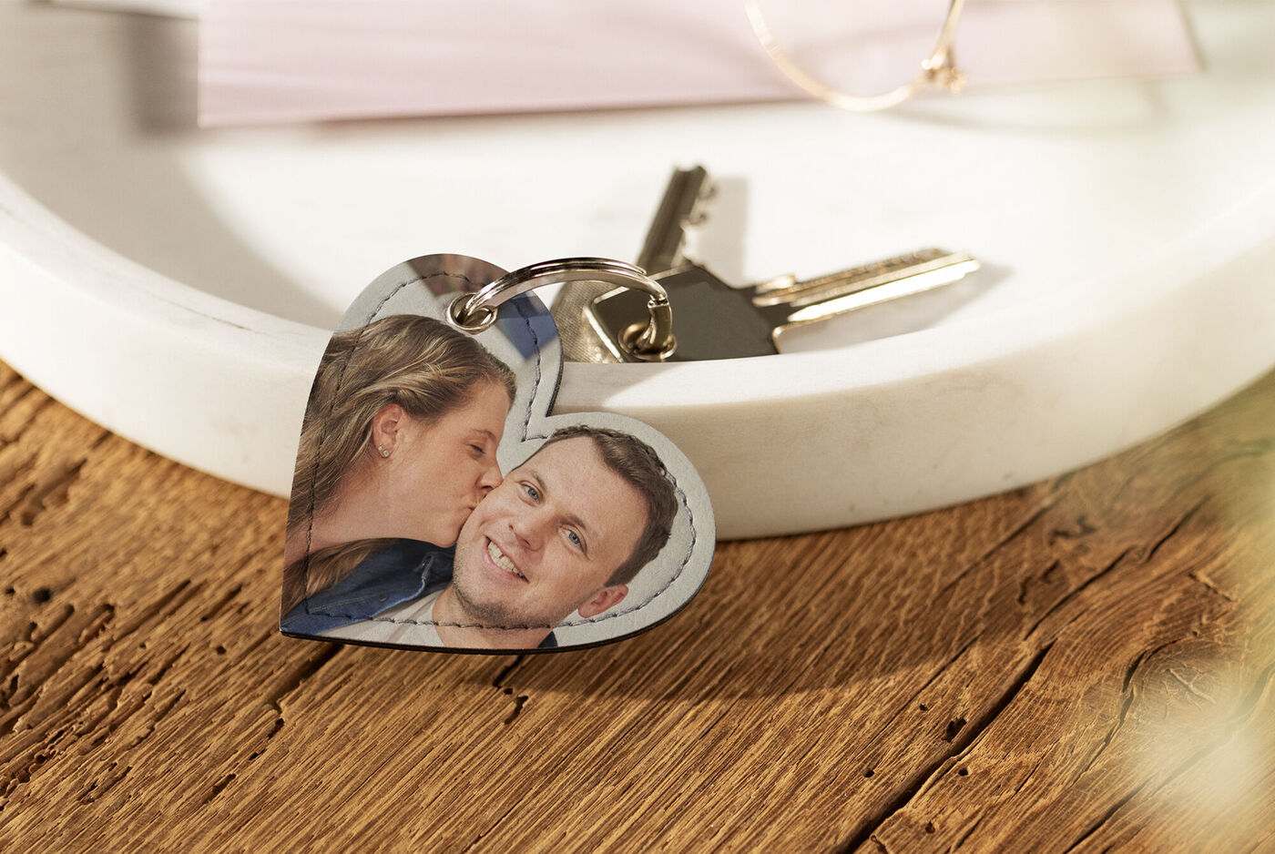 A heart-shaped keychain with a personal photo lying on a wooden table.