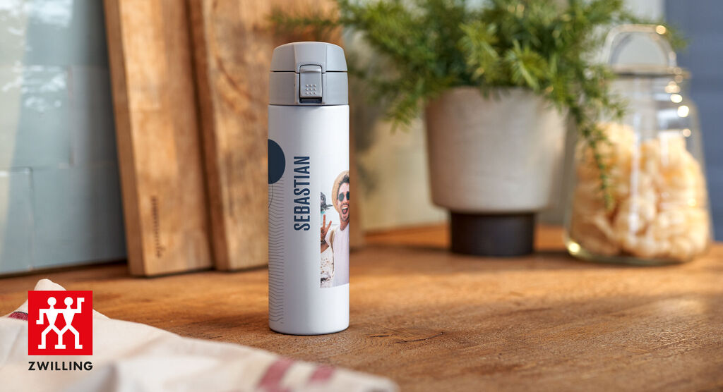 Insulated bottle with photo of Sebastian on a wooden table, surrounded by plants and glasses