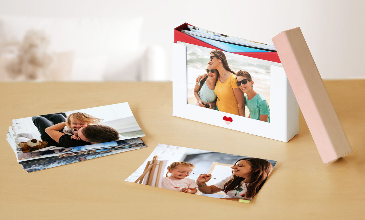Two photo cards on a table, one shows a happy family on the beach, the other a playing mother with child. The card has a heart motif.