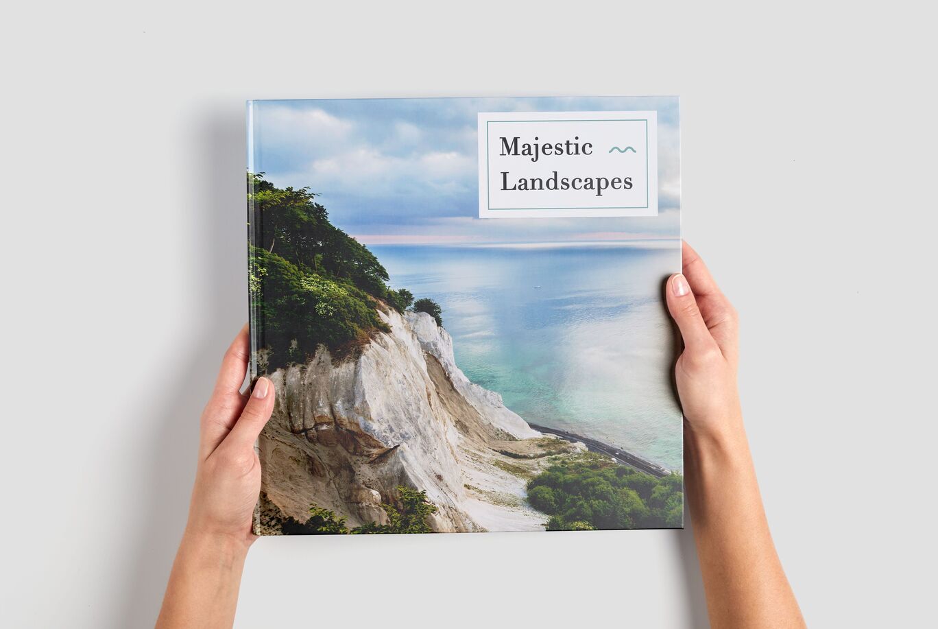 A person holds a CEWE photo book titled 'Majestic Landscapes' against a scenic background.