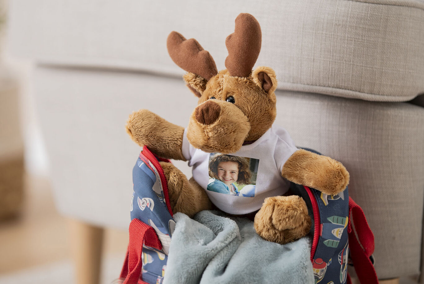 A cute plush reindeer happily sits on a colorful bag, surrounded by a warm blanket