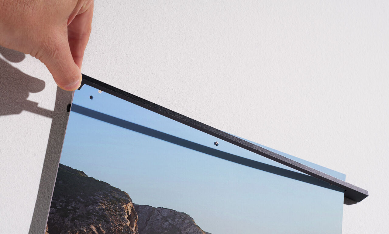 A person hangs a CEWE wall picture. The picture shows a landscape.