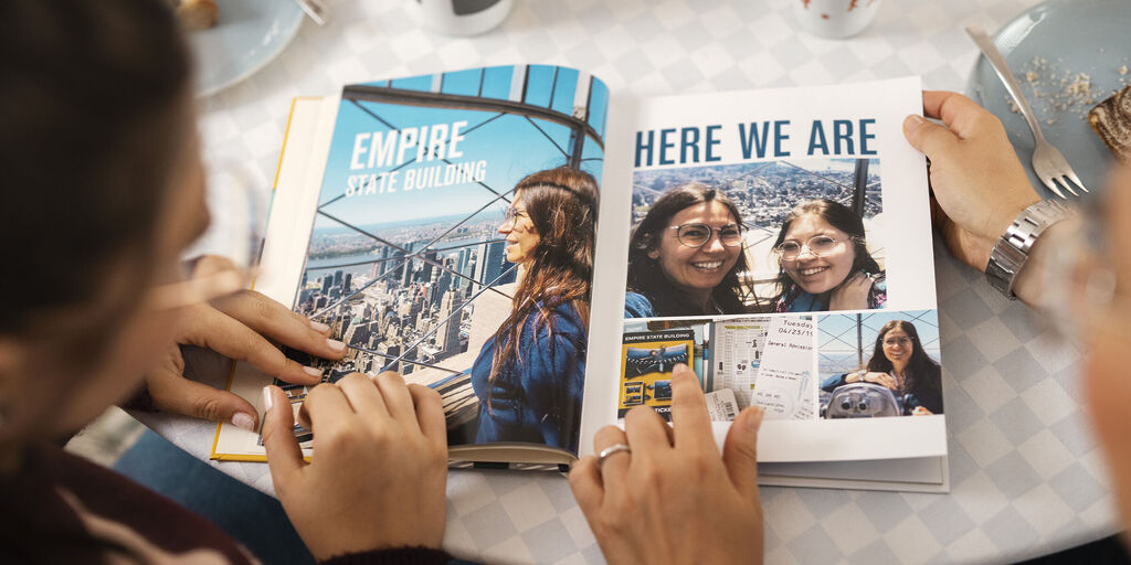 Two people flipping through a photo book with memories from vacation and the Empire State Building