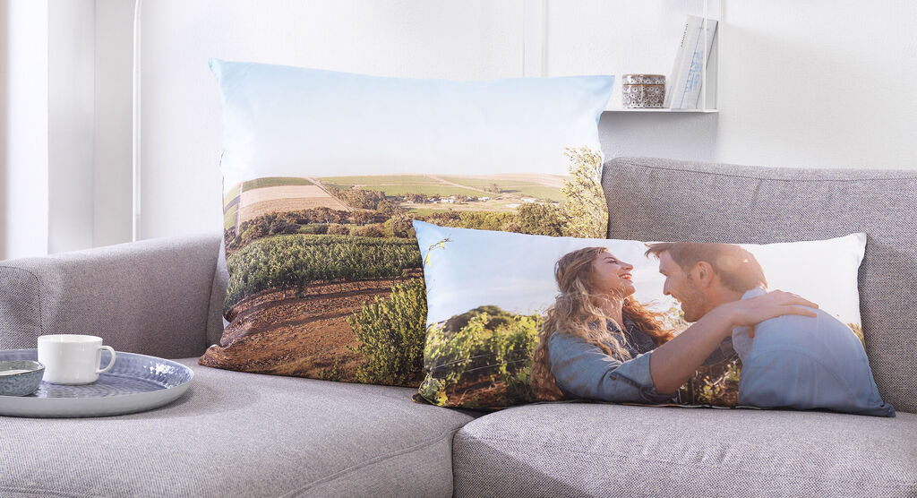 Two cushions with landscape and couple designs on a sofa.