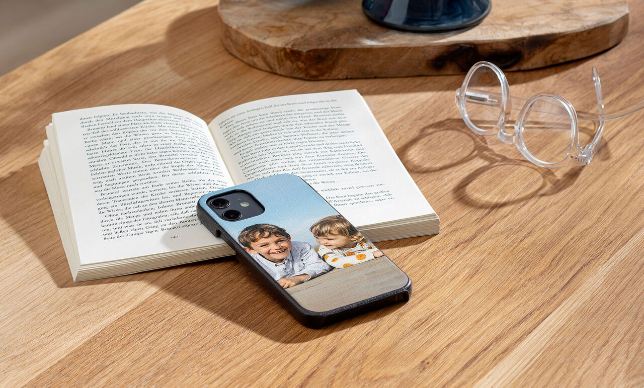 An open book on a table with a smartphone and two laughing children on the cover. Glasses nearby.