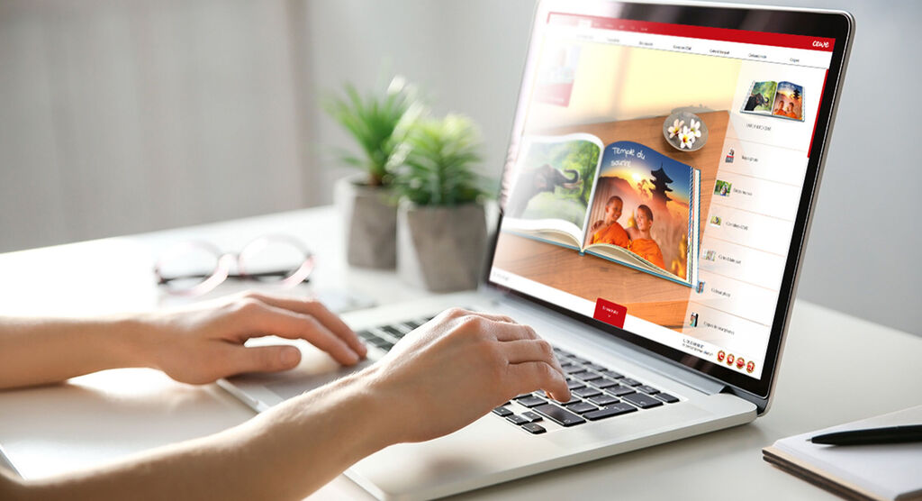 Person working on a laptop, displaying a CEWE photo book on the screen.