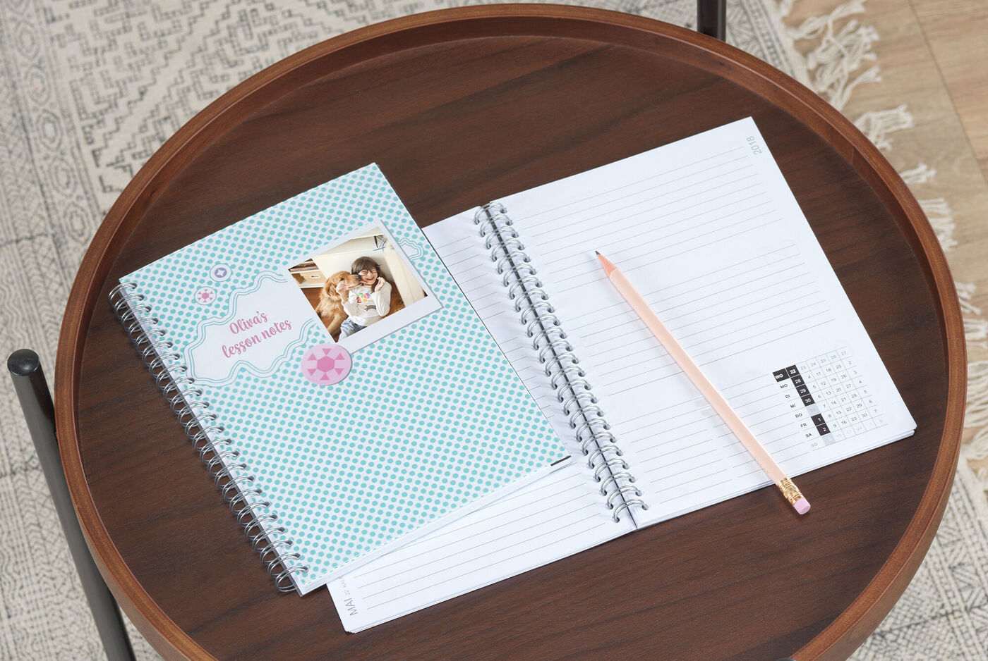 Two notebooks on a table, one with a photo and colorful design, the other empty with a pencil beside it.