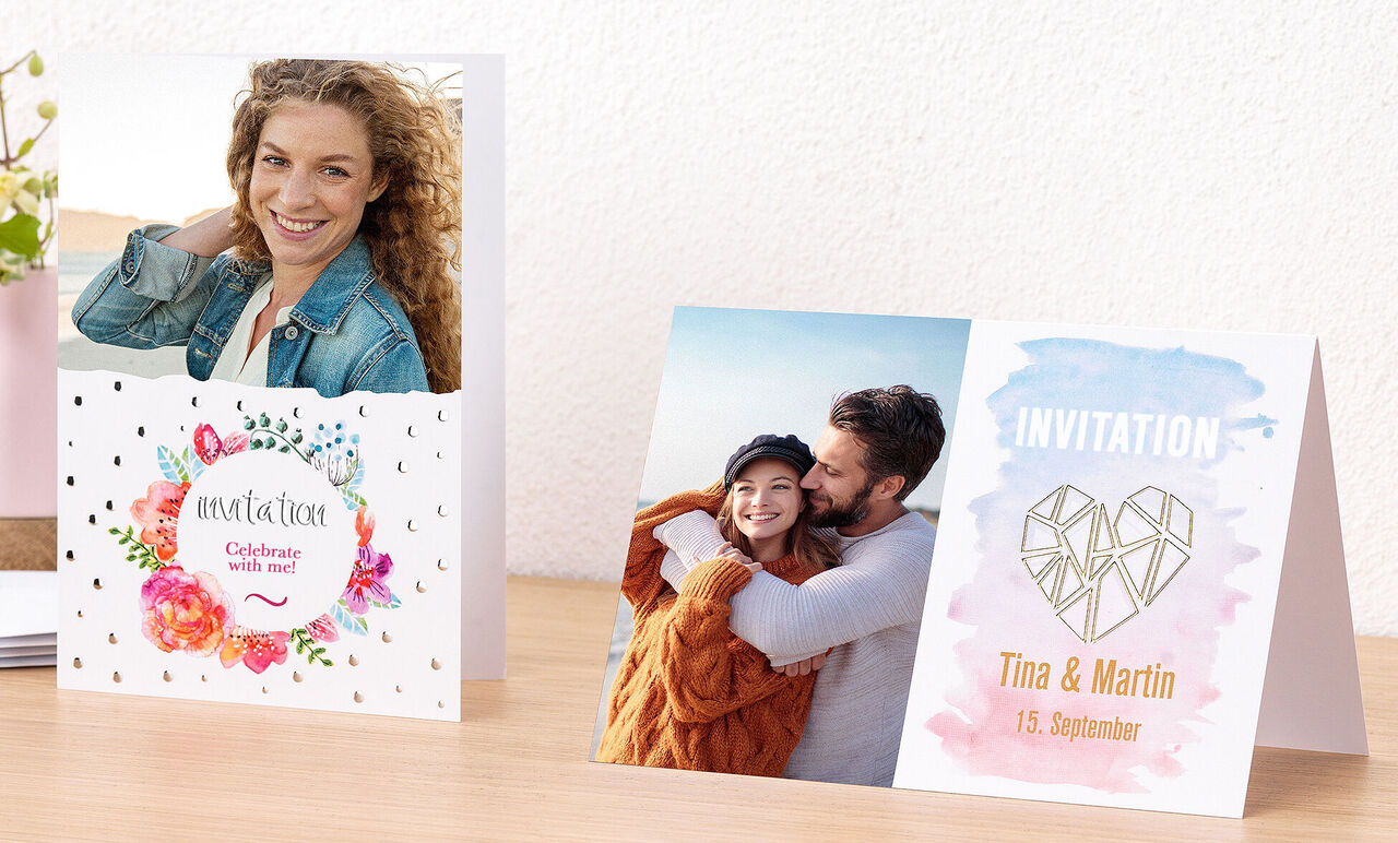 Two colorful invitations on a table, one with flowers and the other with geometric design.
