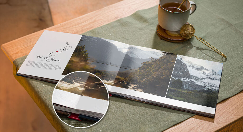 An open CEWE PHOTO BOOK lies on a table next to a cup of tea and a teaspoon.