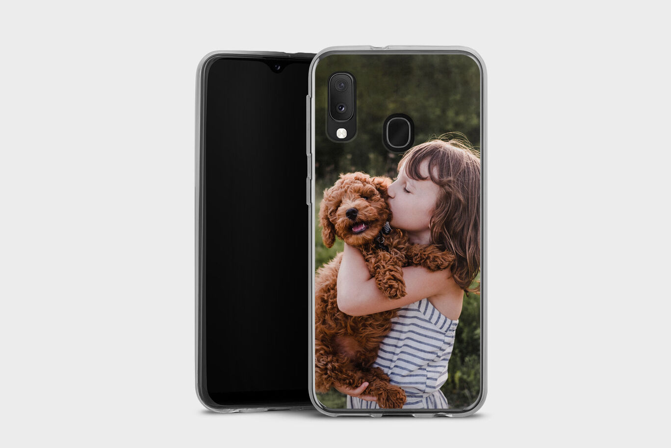 A girl hugs a small brown dog with curly fur, both beaming with joy. A green meadow in the background.
