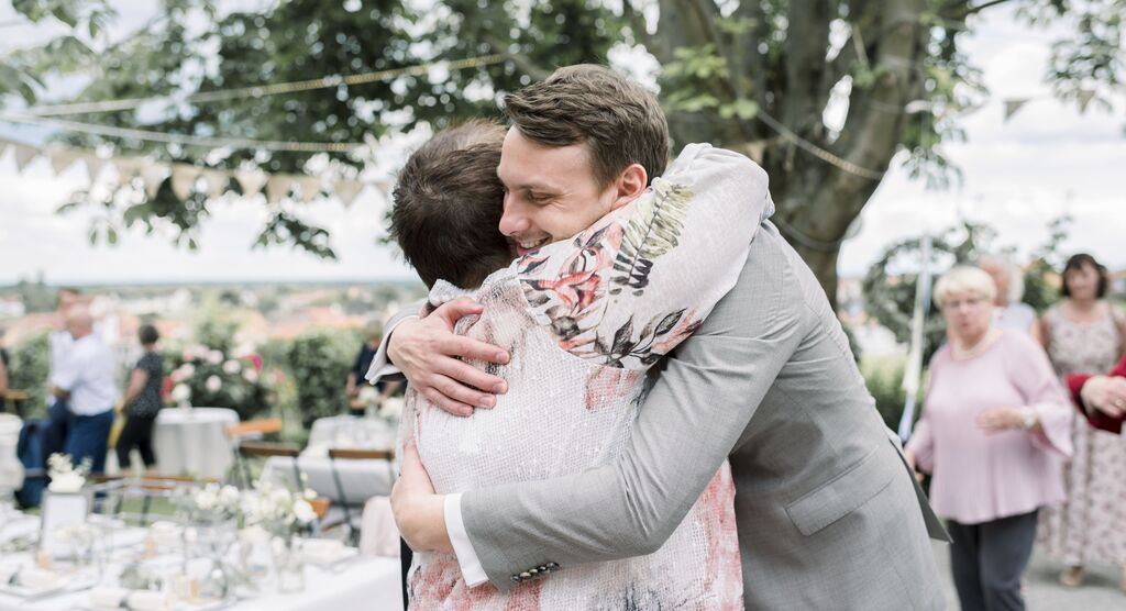 Two people warmly embrace at a celebration with festive decorations in the background.