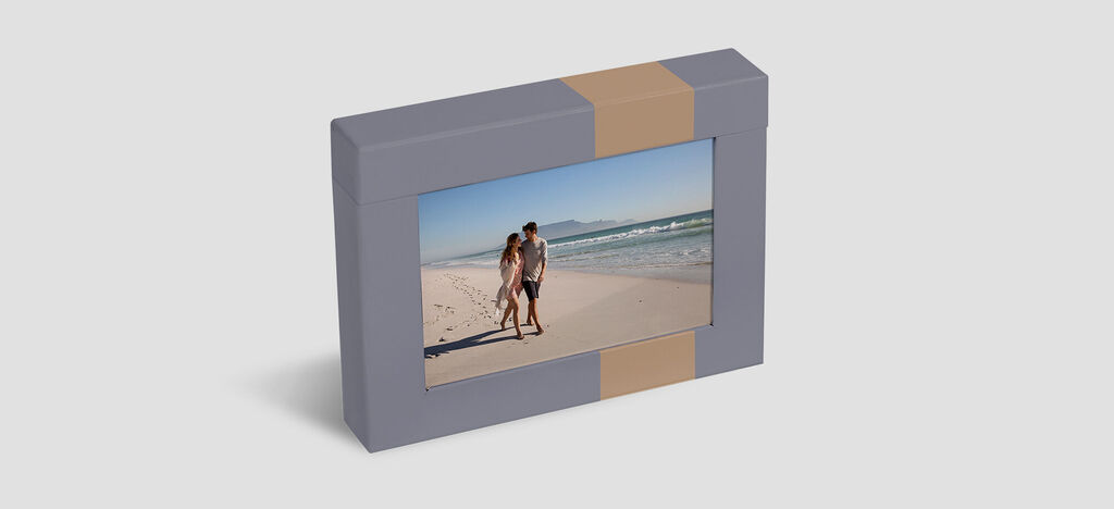 A happy couple stands on the beach holding a photo in an attractive frame.
