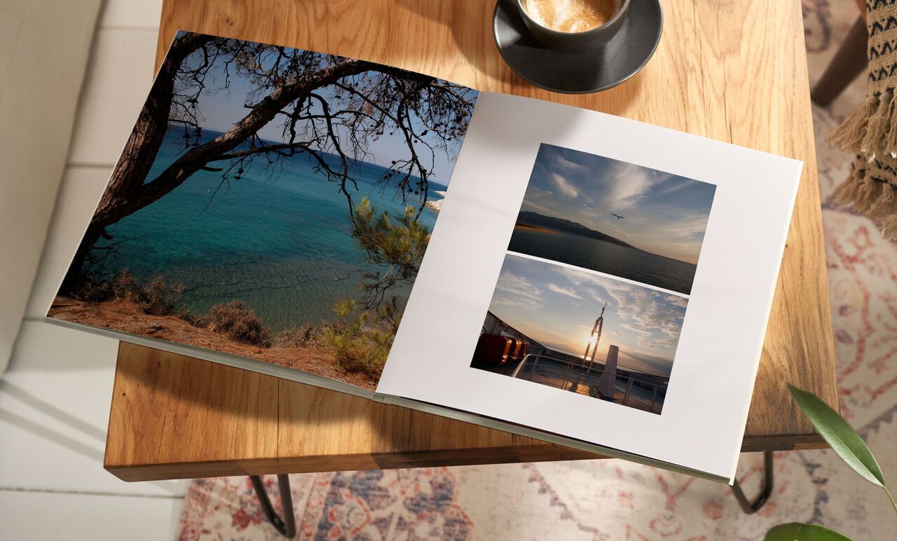 Open photo book on a table with dreamy vacation images. A sea blue image above, two below showing sailboats and a sunset.