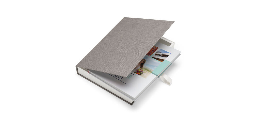 An open CEWE PHOTOBOOK with colorful photos and a gray surface