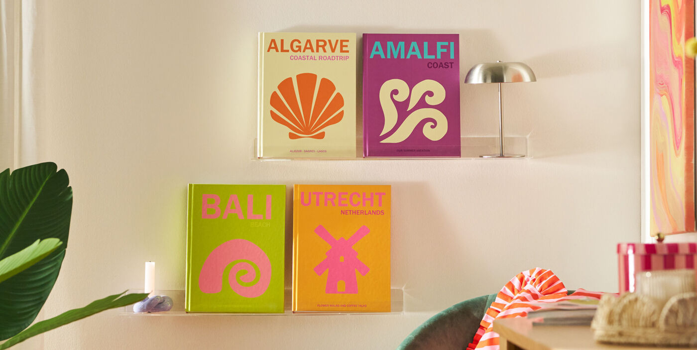 Four different travel coffee table books from different places are standing on a wall shelf in a colourful living room environment.