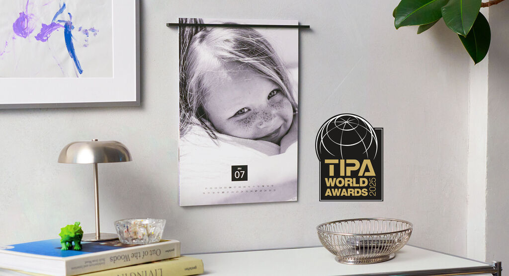 A beautiful calendar hangs on a wall. On a table, there are a lamp, books, and a basket.