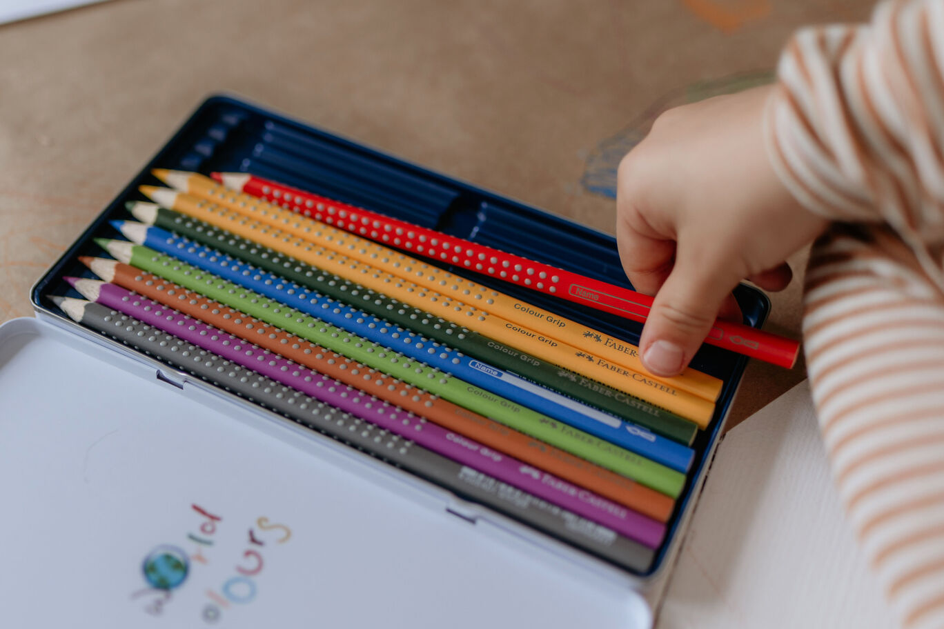 Colorful pencils in a tin can, a child reaches for a red pencil.