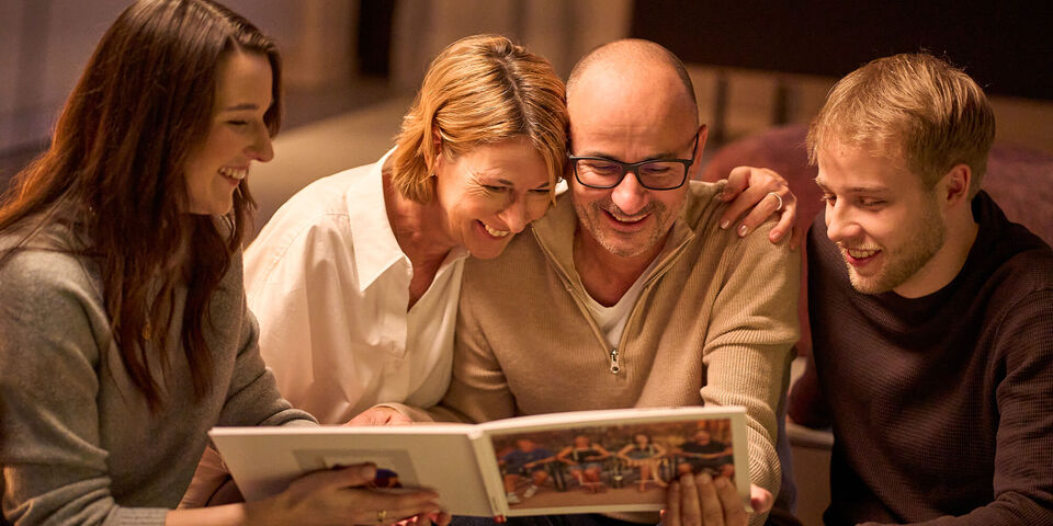 Family looks at a photo book about their vacation and shares special memories together.