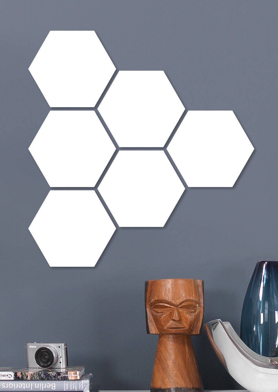 Six white hexagonal shapes on a gray wall, next to a modern lamp and a camera