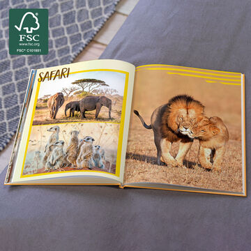 An open photo book with animal motifs from a safari adventure. Elephants and meerkats are on the left, two lions close together on the right.