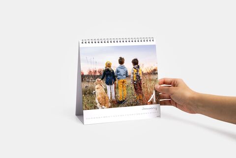 Three children standing with a dog on a meadow at sunset, holding a calendar.