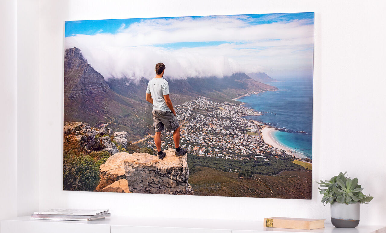 Man stands on a cliff and looks at a coastal landscape with a city and mountains