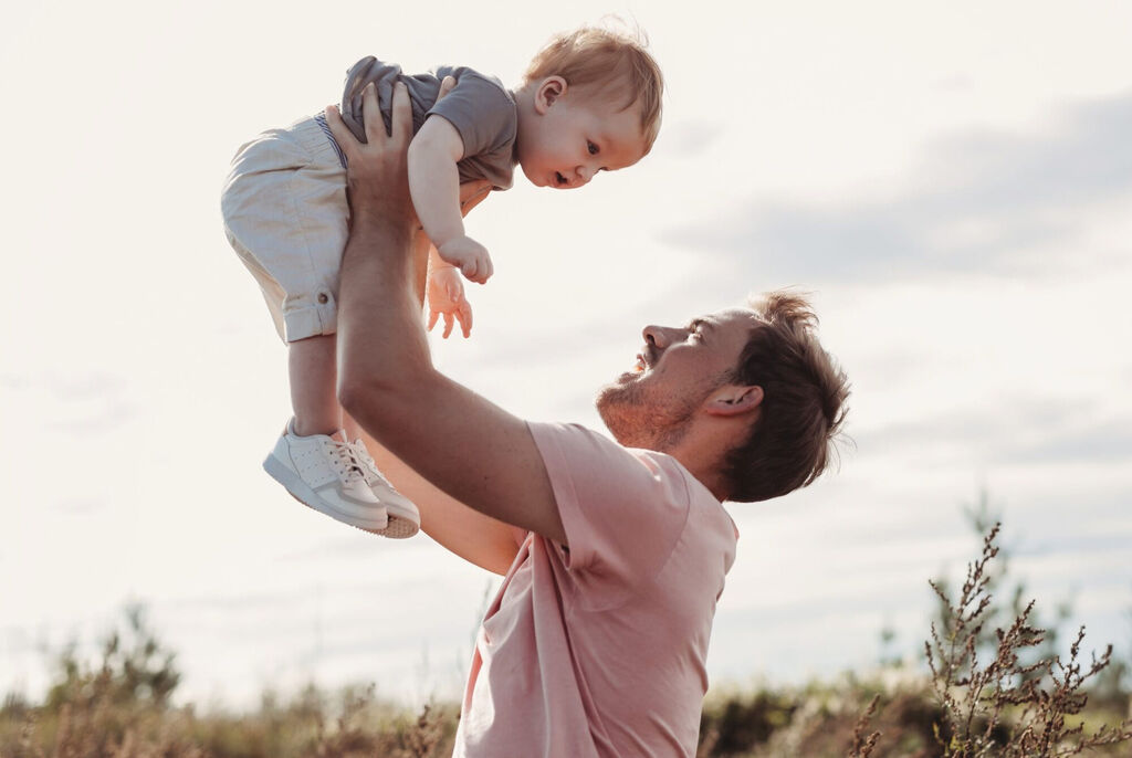 Father joyfully lifts his child into the air, surrounded by beautiful nature.