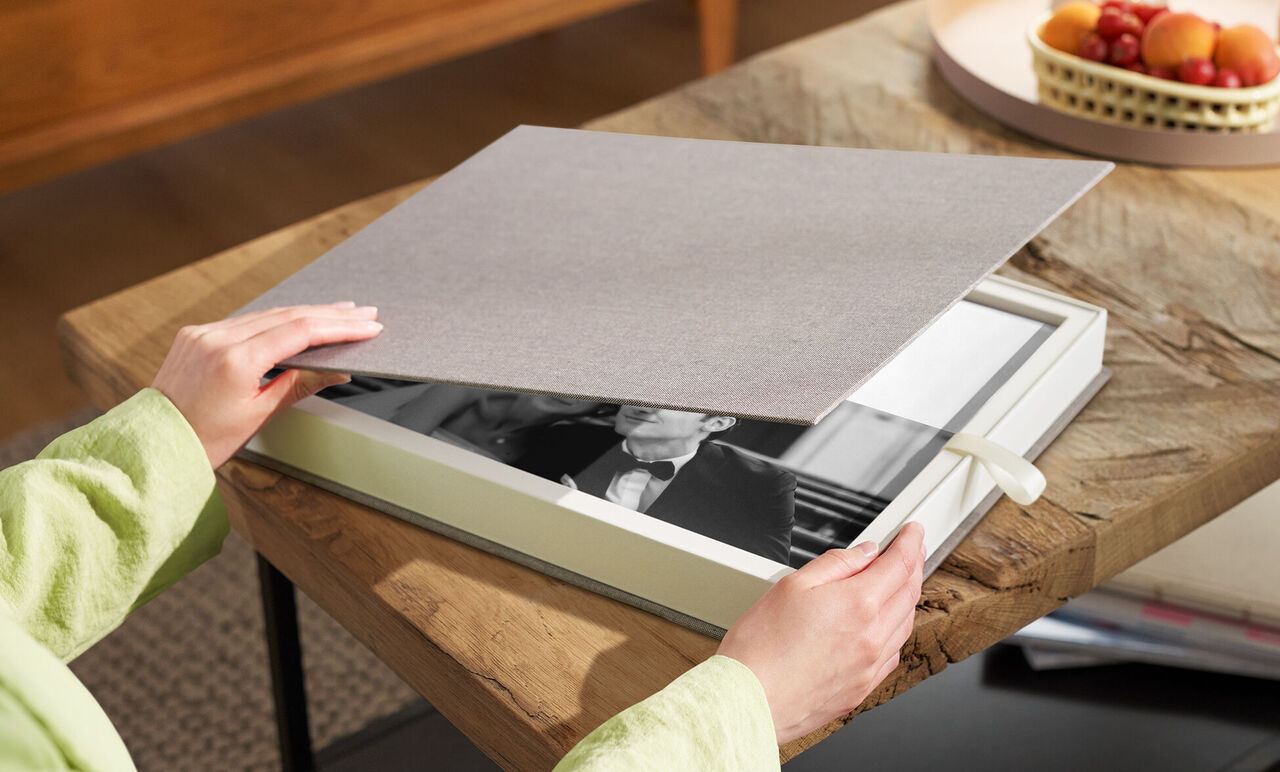A person opens a CEWE photo book on a wooden table.