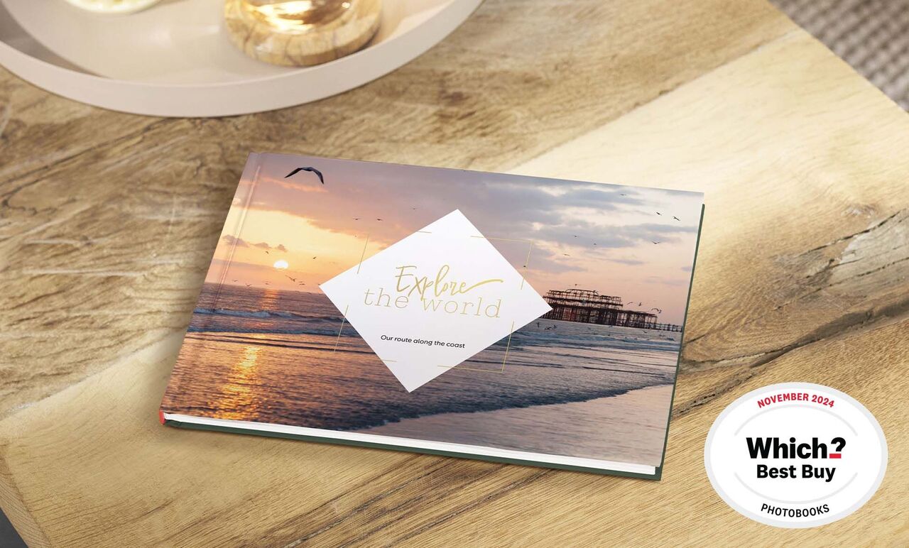 A beautiful CEWE PHOTO BOOK lying on a wooden table showing a sunset over the water.