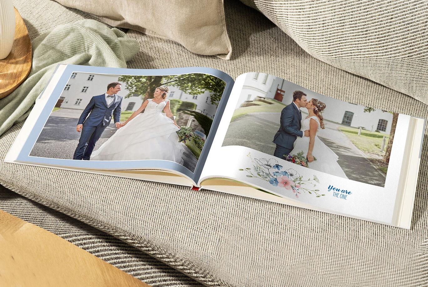 An opened CEWE PHOTO BOOK on a cozy couch with wedding photos and floral designs.
