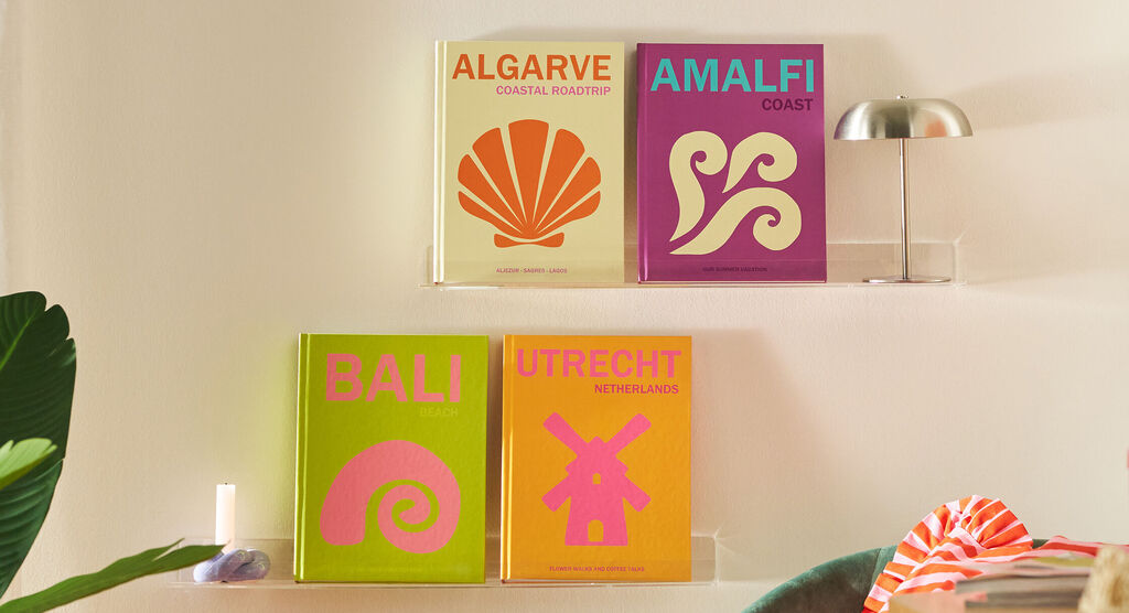 Four different travel coffee table books from different places are standing on a wall shelf in a colourfull living room enviroment.
