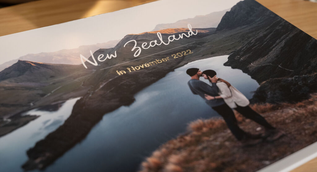 A couple embraces by the water in New Zealand, surrounded by mountains.