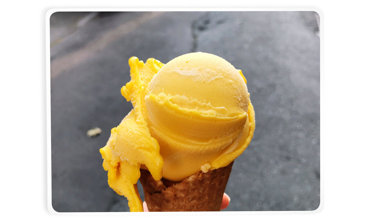 Scoop of yellow sorbet on a cone in hand.