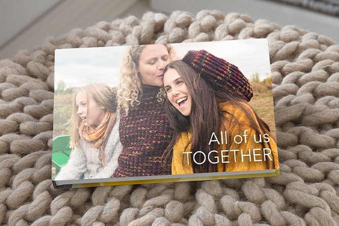 Three friends enjoy time together outdoors with a CEWE PHOTO BOOK on a cozy surface.