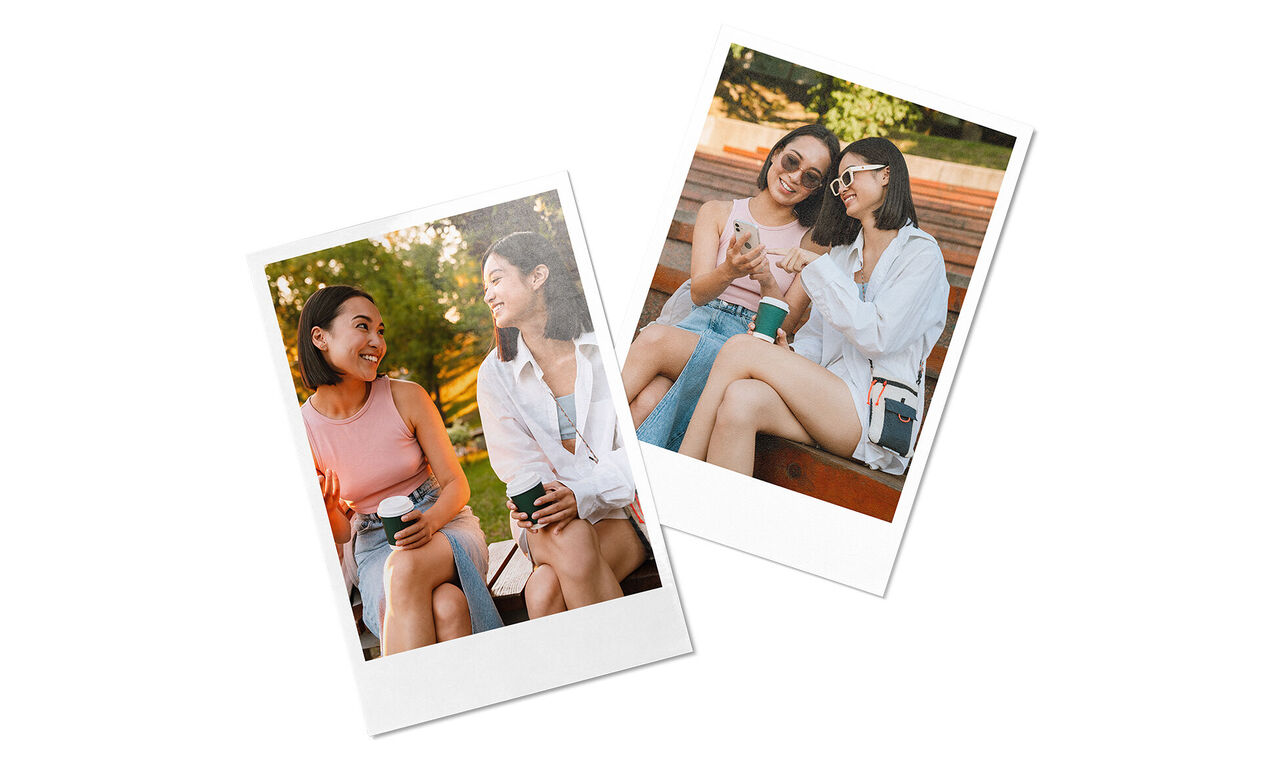 Two women sit in the park chatting. One holds a coffee cup.