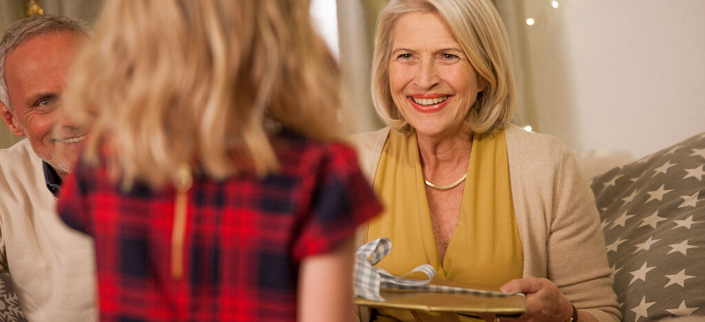 A happy child hands a gift to an adult in a festive room.