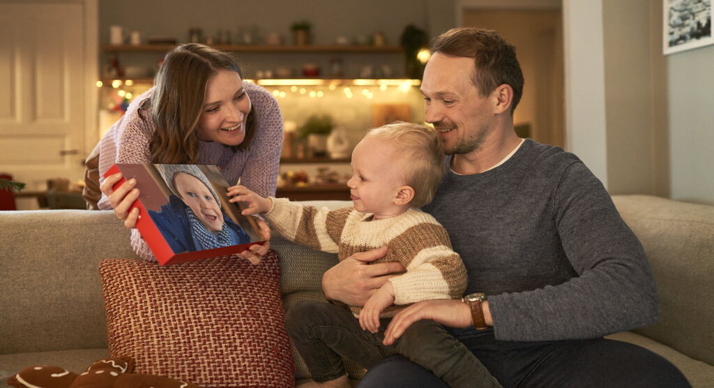 Family holding a photo book with a child's image while sitting together on the sofa.