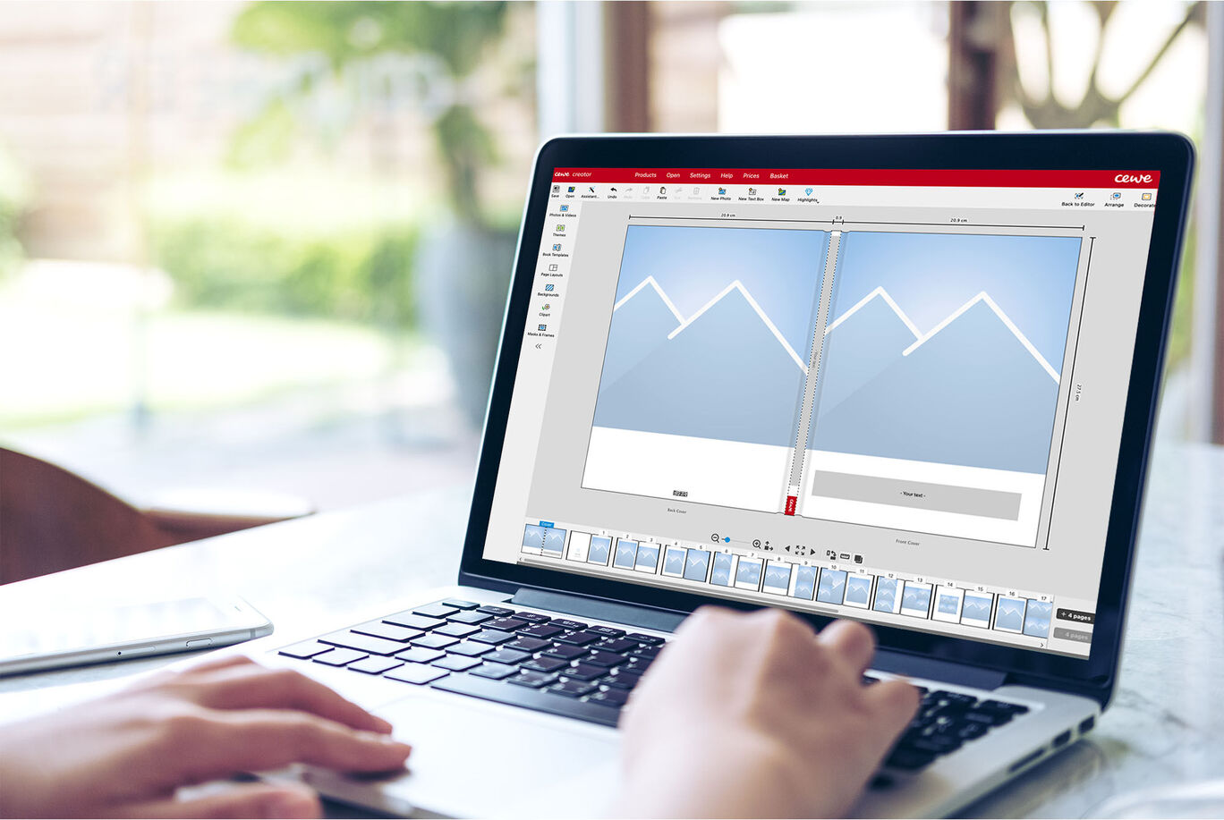 A person designing a CEWE PHOTO BOOK on a laptop with a graphic background in bright colors