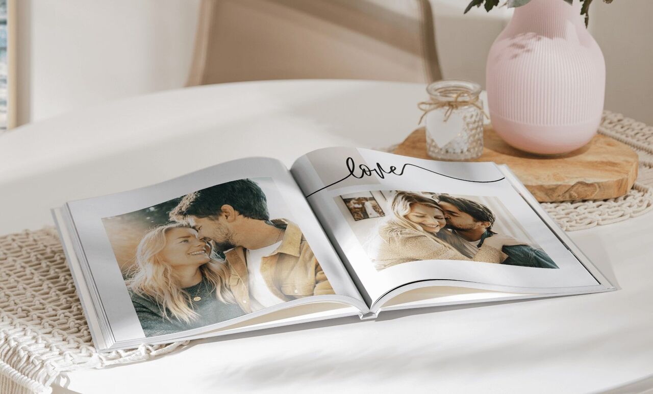 Open photo book on a table features two images of a couple and the word 'love'.