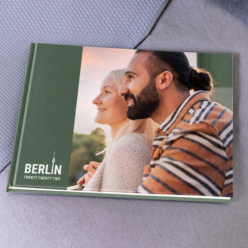 A couple sits together on a sofa looking content into the distance. Their loving connection is visible. In the background is a photo book titled "Berlin."