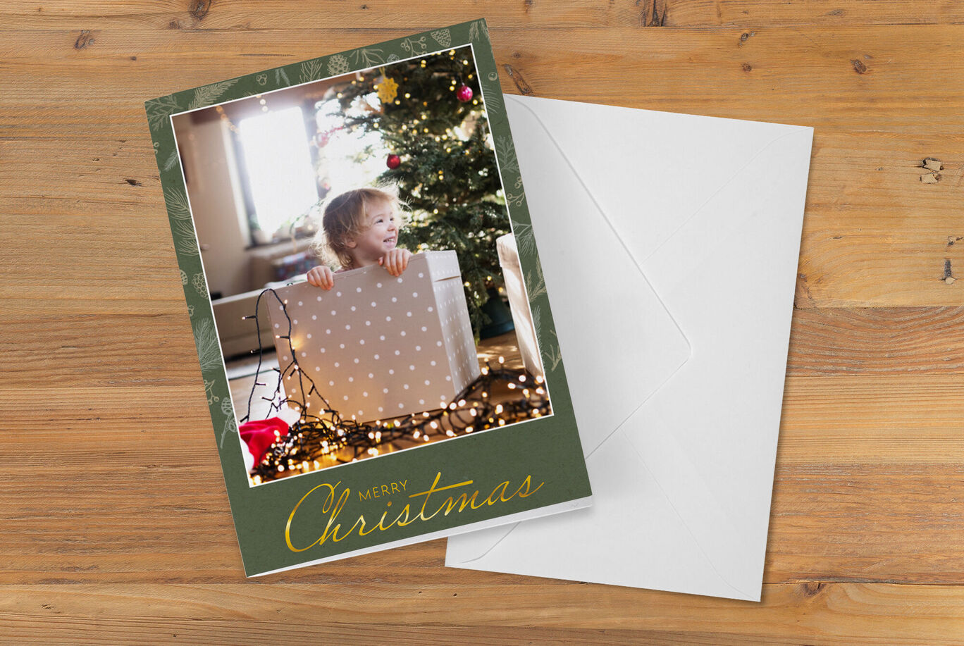 A child holds a big gift in front of a Christmas tree with lights.