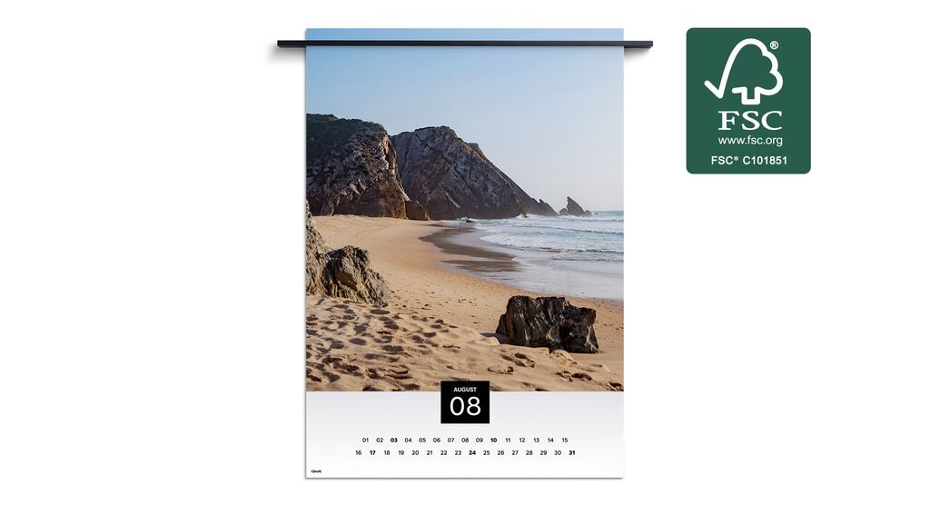 Beach landscape with rocks and gentle waves under a blue sky, shown in a wall calendar for August.